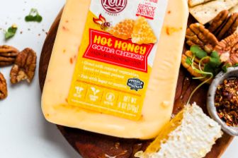 A block of Roth Hot Honey Gouda cheese displayed on a wooden board alongside honeycomb, pecans, crackers, sliced cheese, herbs, and seasoning, creating a vibrant and appetizing cheese‑board presentation.