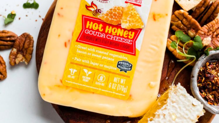 A block of Roth Hot Honey Gouda cheese displayed on a wooden board alongside honeycomb, pecans, crackers, sliced cheese, herbs, and seasoning, creating a vibrant and appetizing cheese‑board presentation.