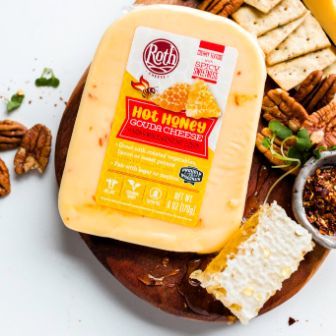 A block of Roth Hot Honey Gouda cheese displayed on a wooden board alongside honeycomb, pecans, crackers, sliced cheese, herbs, and seasoning, creating a vibrant and appetizing cheese‑board presentation.