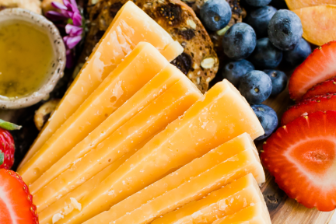 A close‑up view of an artisan cheeseboard featuring neatly arranged wedges of aged gouda surrounded by fresh strawberries, blueberries, crisp crackers, and a small bowl of honey.